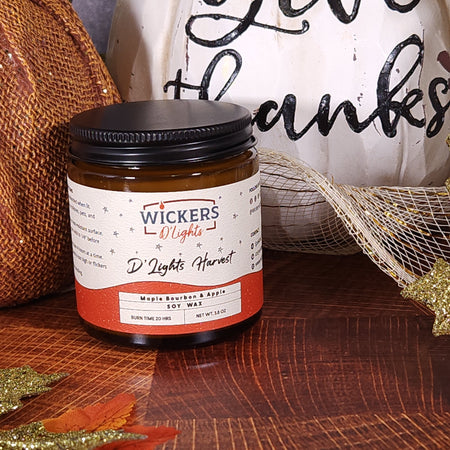 A close-up of a Wickers D'Lights Harvest 3.8oz soy wax jar with maple bourbon and apple scent, prominently placed in front of a decorative 'thanks' sign, with a hessian ribbon and golden glitter leaves on a rich wooden table, creating a warm Thanksgiving theme.